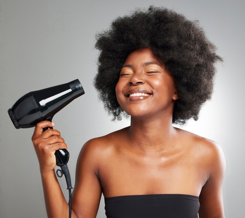 Black woman smiling while blow drying her natural afro hair